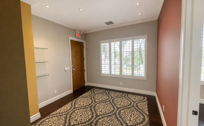 Modern office space with patterned carpet, wood floors, and large window with plantation shutters.